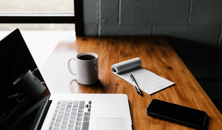 MacBook Pro, white ceramic mug,and black smartphone on table