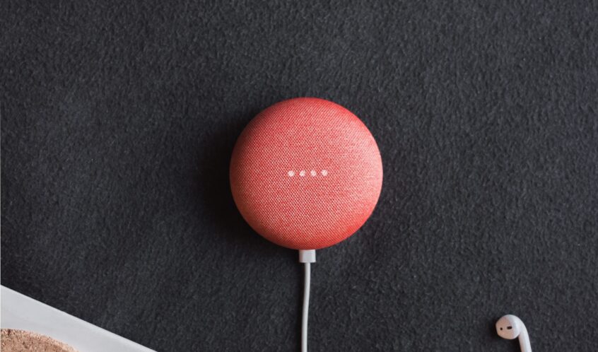 flat lay photography of coral Google Home Mini on black surface beside Apple AirPods